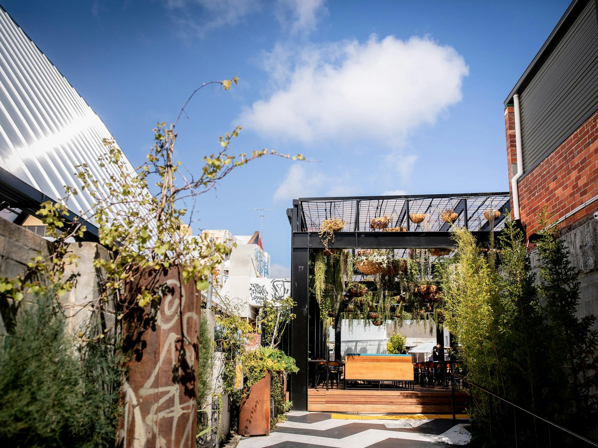 A black and white path leads into a wood decked bar area, plants hang from the ceiling