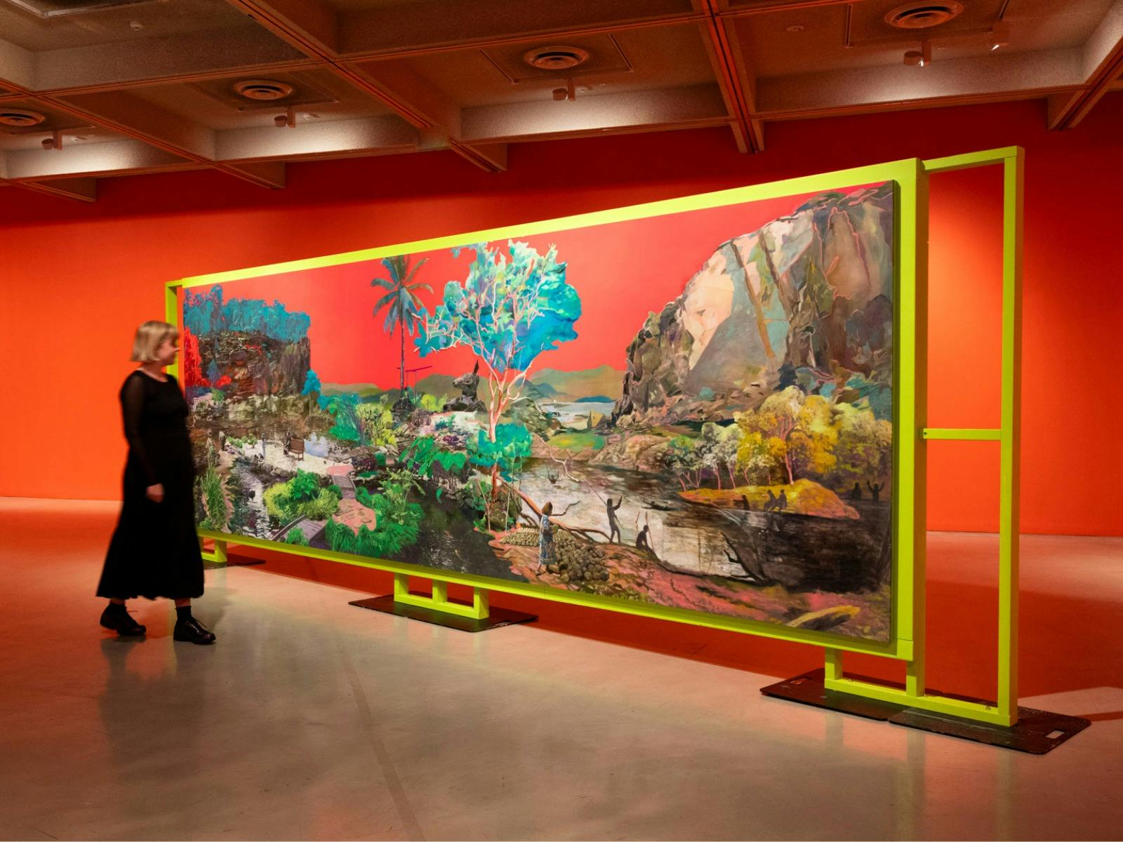 Gallery space with bright orange walls and large-scale landscape painting of bright neon colours