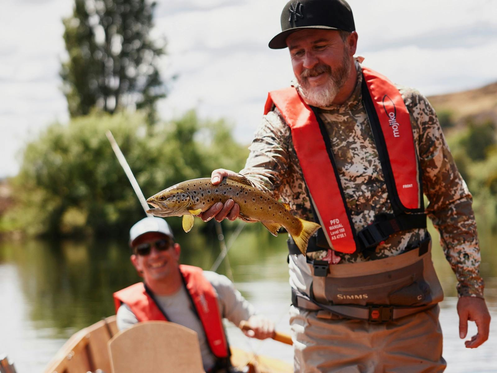 Marcus Saunders holding up a Brown trout in his drift boat, Tasmania