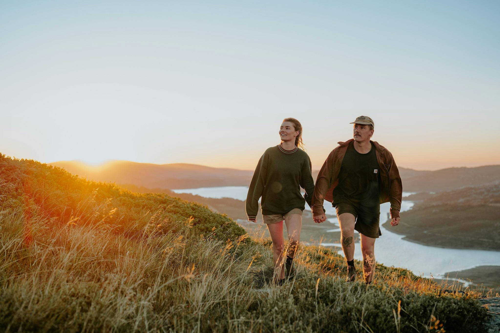 A couple walk hand in hand through the grass near Rokey Valley on a clear summer morning at sunrise.