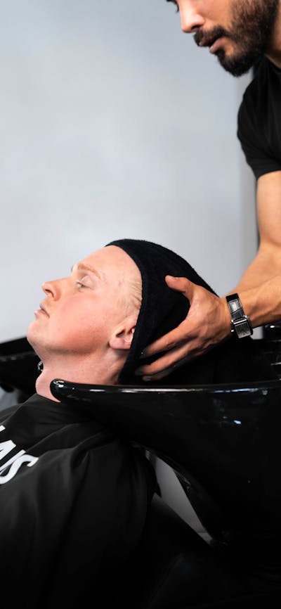 A client relaxing in a barber wash station while receiving a scalp treatment and head massage