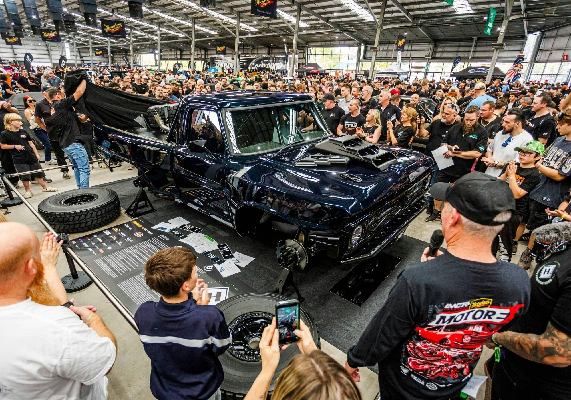 Dark blue custom pickup being unveiled before a large indoor crowd at MotorEx.
