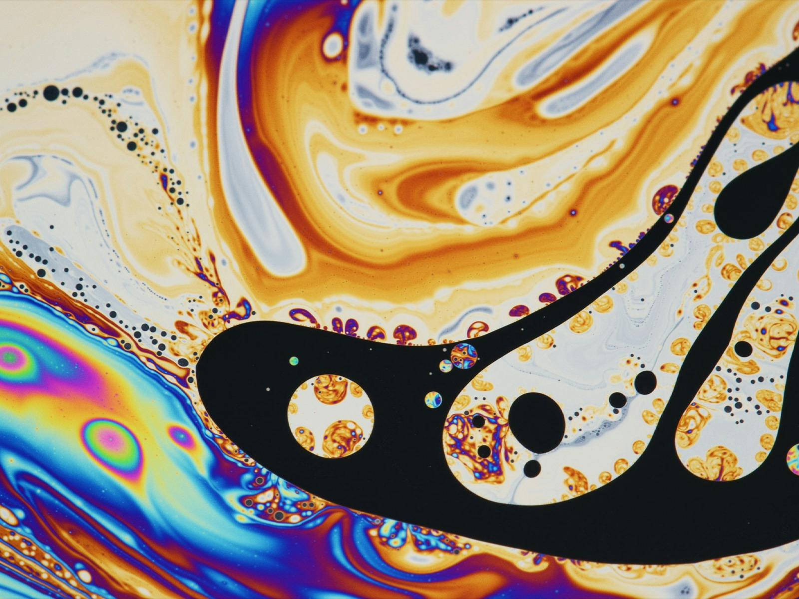 Swirling orange, blue and black liquid forming abstract shapes and bubbles.
