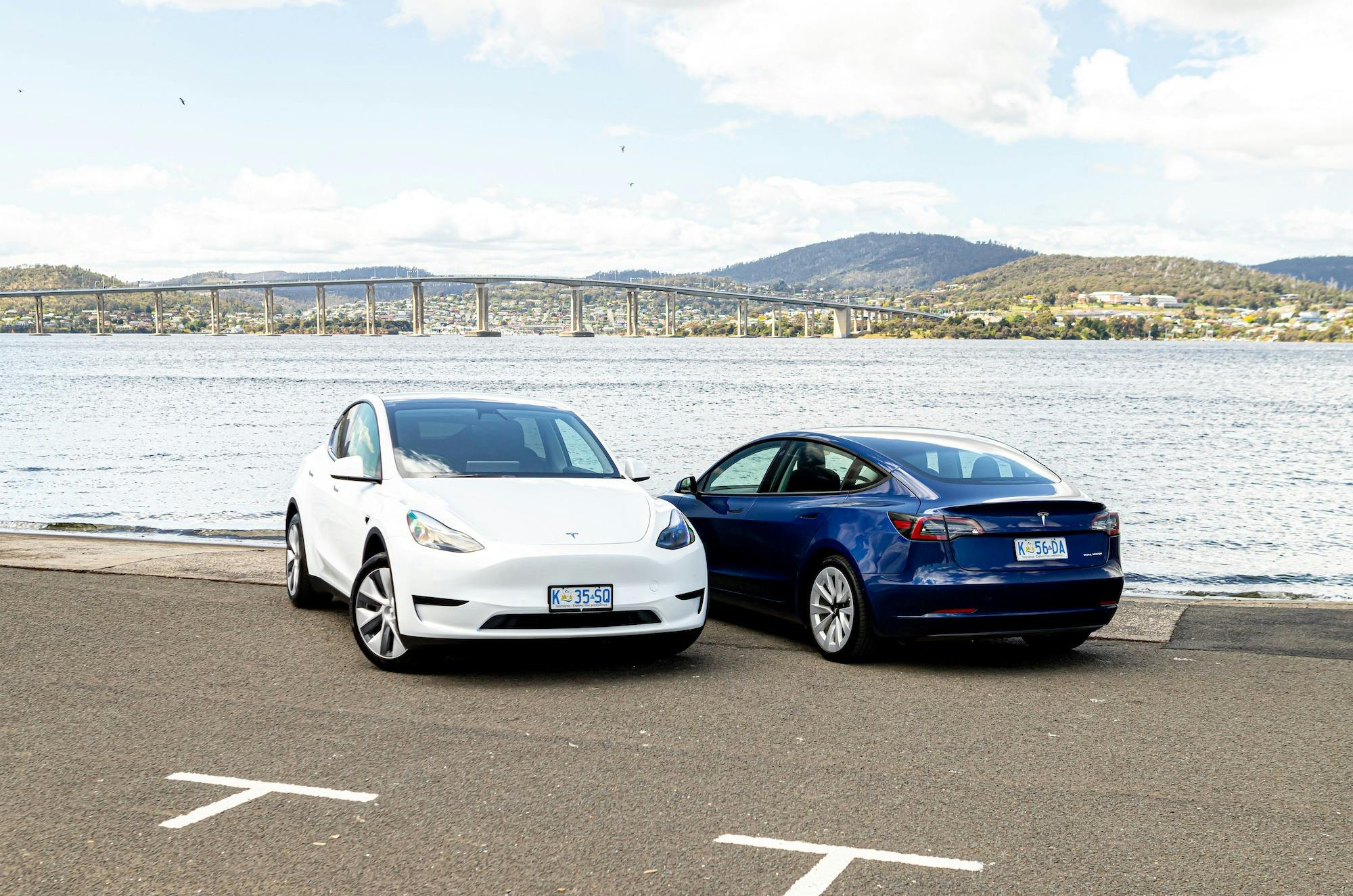 A white Tesla Model Y and blue Tesla Model 3 parked beside each other next to the Derwent River