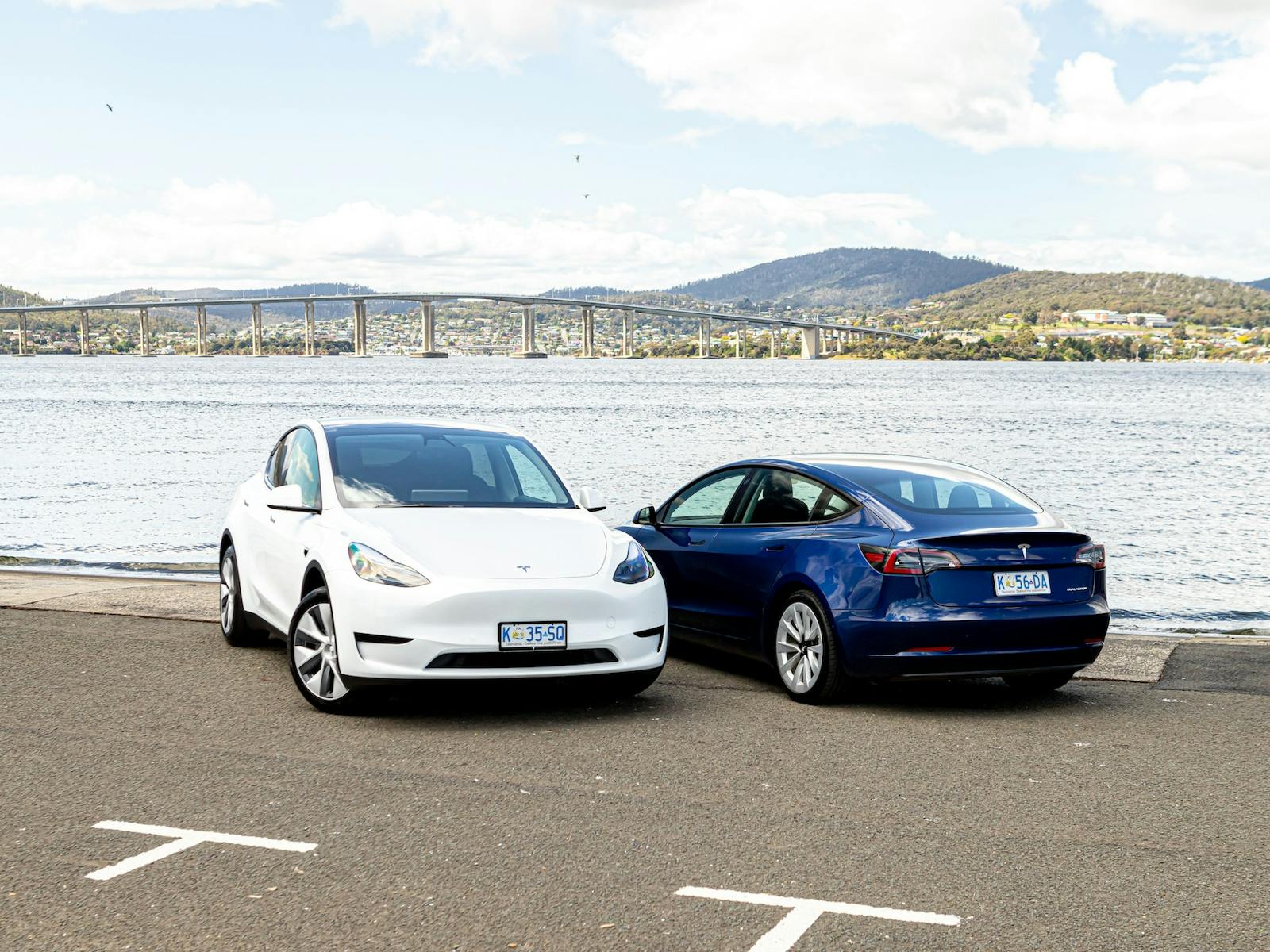 A white Tesla Model Y and blue Tesla Model 3 parked beside each other next to the Derwent River