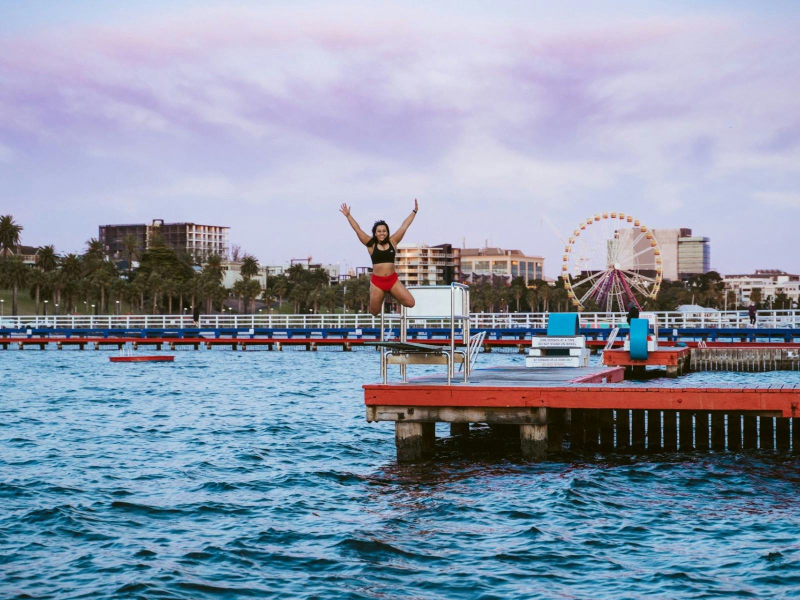 Girl jumping off the dock into the water with hands up in the air