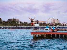 Girl jumping off the dock into the water with hands up in the air