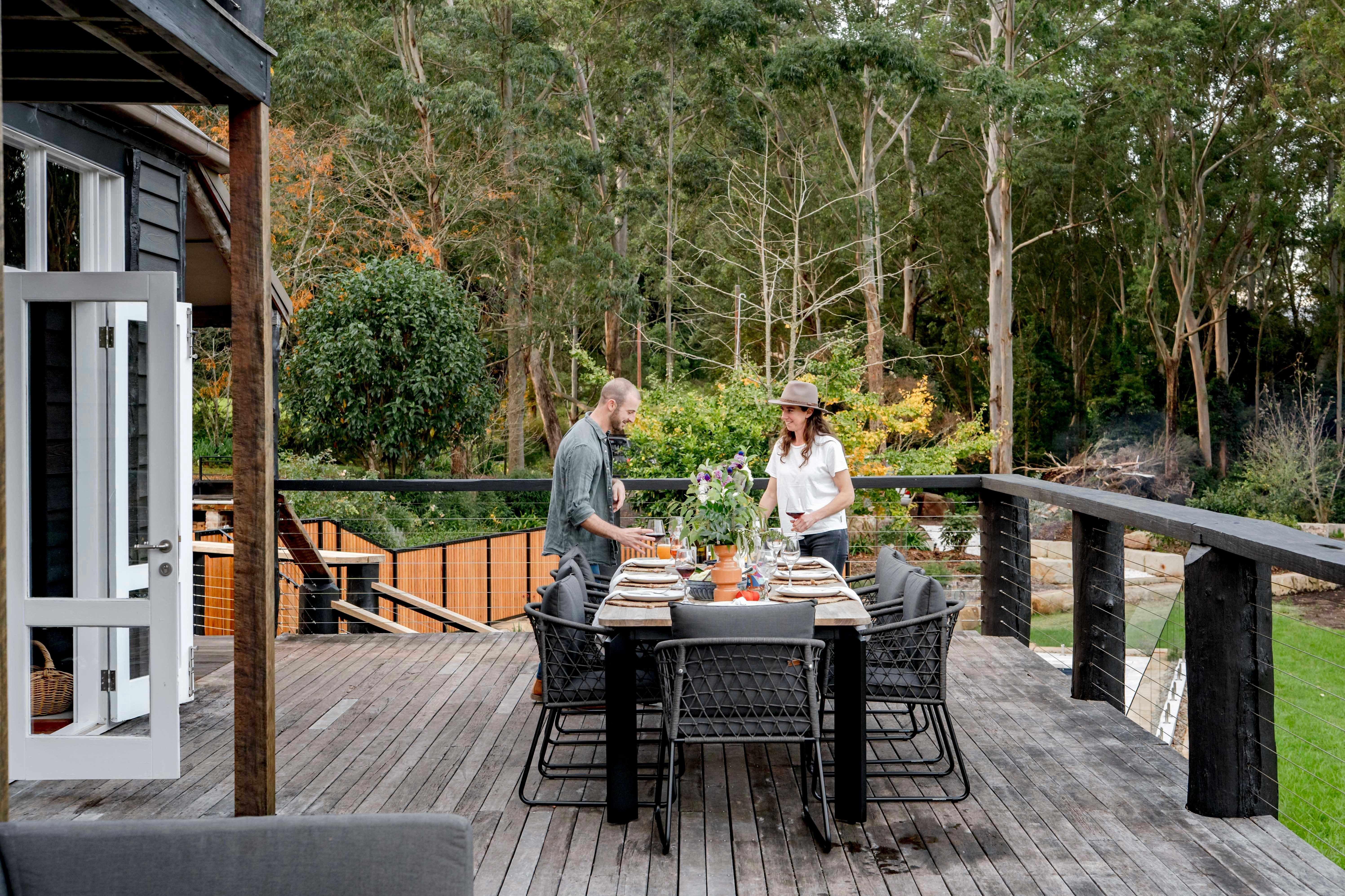 two people setting an outdoor table on a deck overlooking gardens