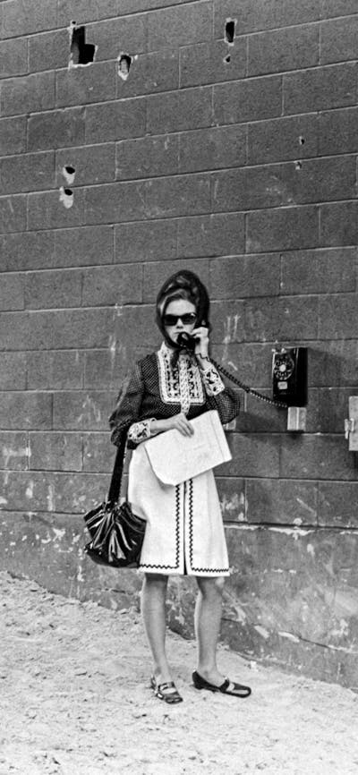 black and white photo of texas in the 170's. a woman is at an old phone booth and cowboys lead horse