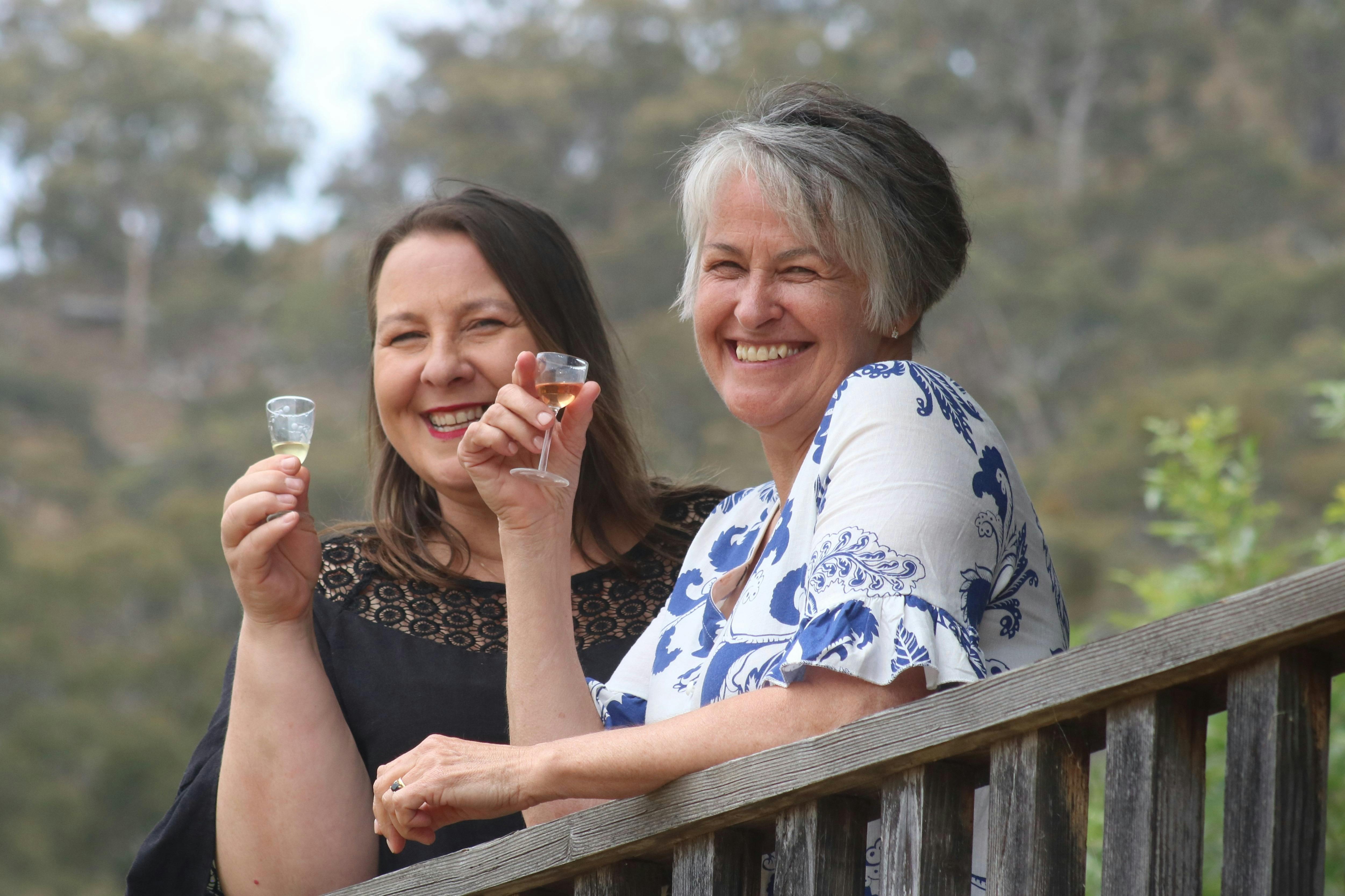 Two women smiling, raising gin liqueur glasses