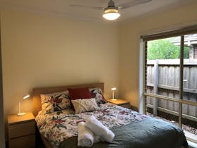 Bedroom with queen sized bed, bedside tables with lamps and large window. Ceiling fan above bed