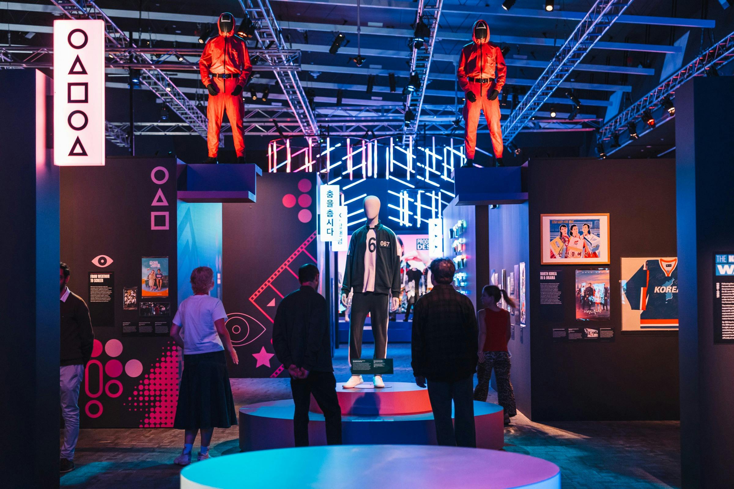 Exhibit with mannequins in red jumpsuits, surrounded by neon lights and displays.