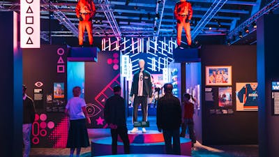 Exhibit with mannequins in red jumpsuits, surrounded by neon lights and displays.