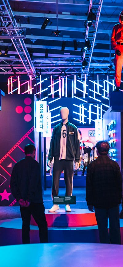 Exhibit with mannequins in red jumpsuits, surrounded by neon lights and displays.