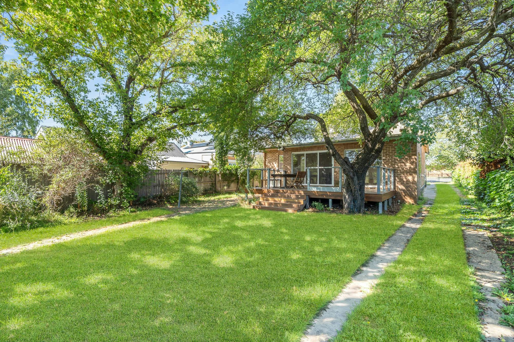 Backyard with grass, lots of trees, verandah with outdoor furniture