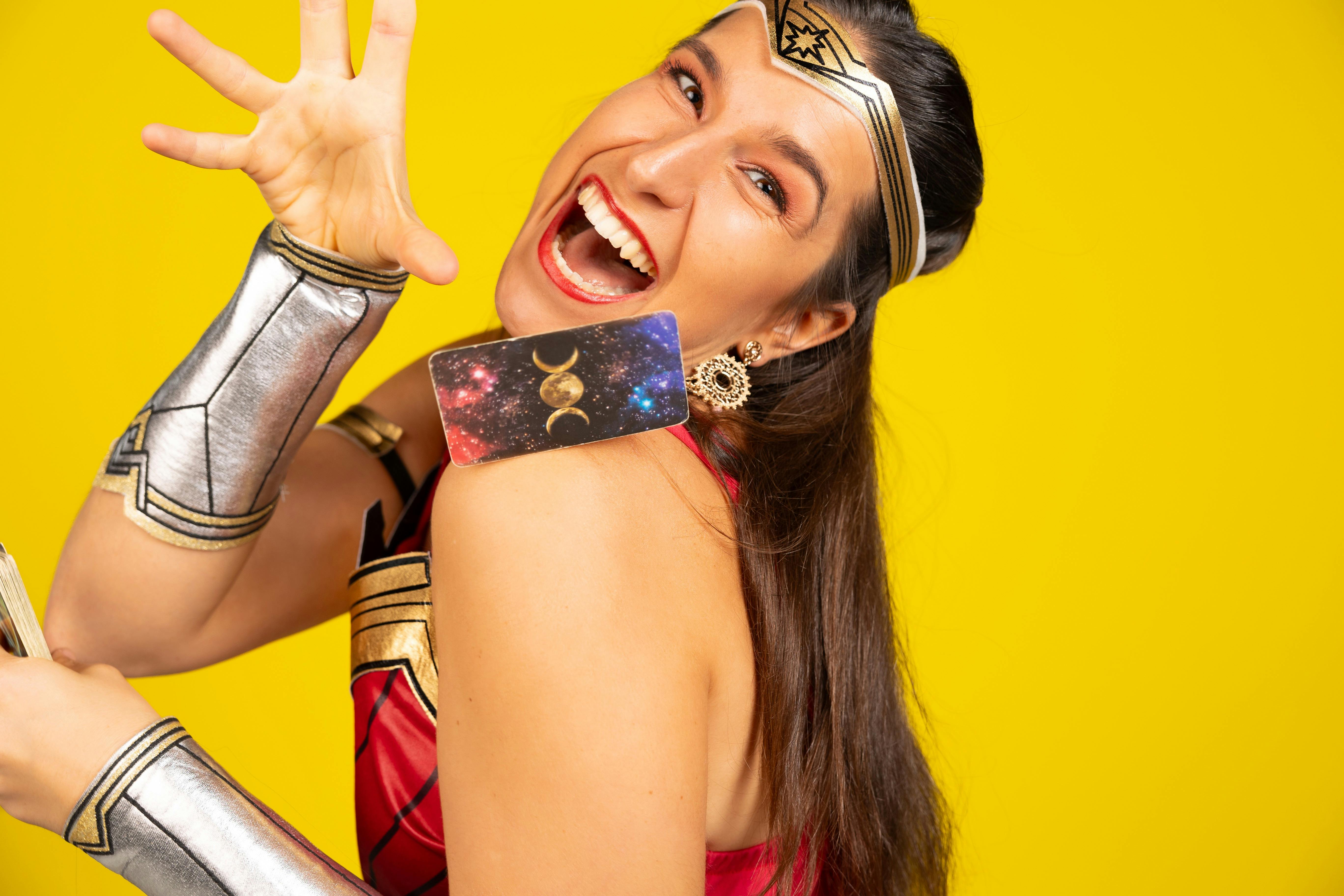 A smiling woman dressed in Wonder Woman with a tarot card 'falling' on top of her shoulder.