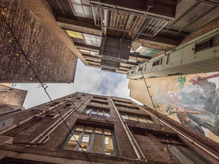 A view looking skyward from the courtyard with 5 story building towering on each side, and a mural.
