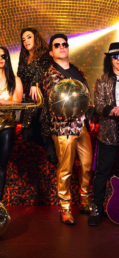 A collection of people in sparkly outfits with instruments with sunglasses looking at the camera