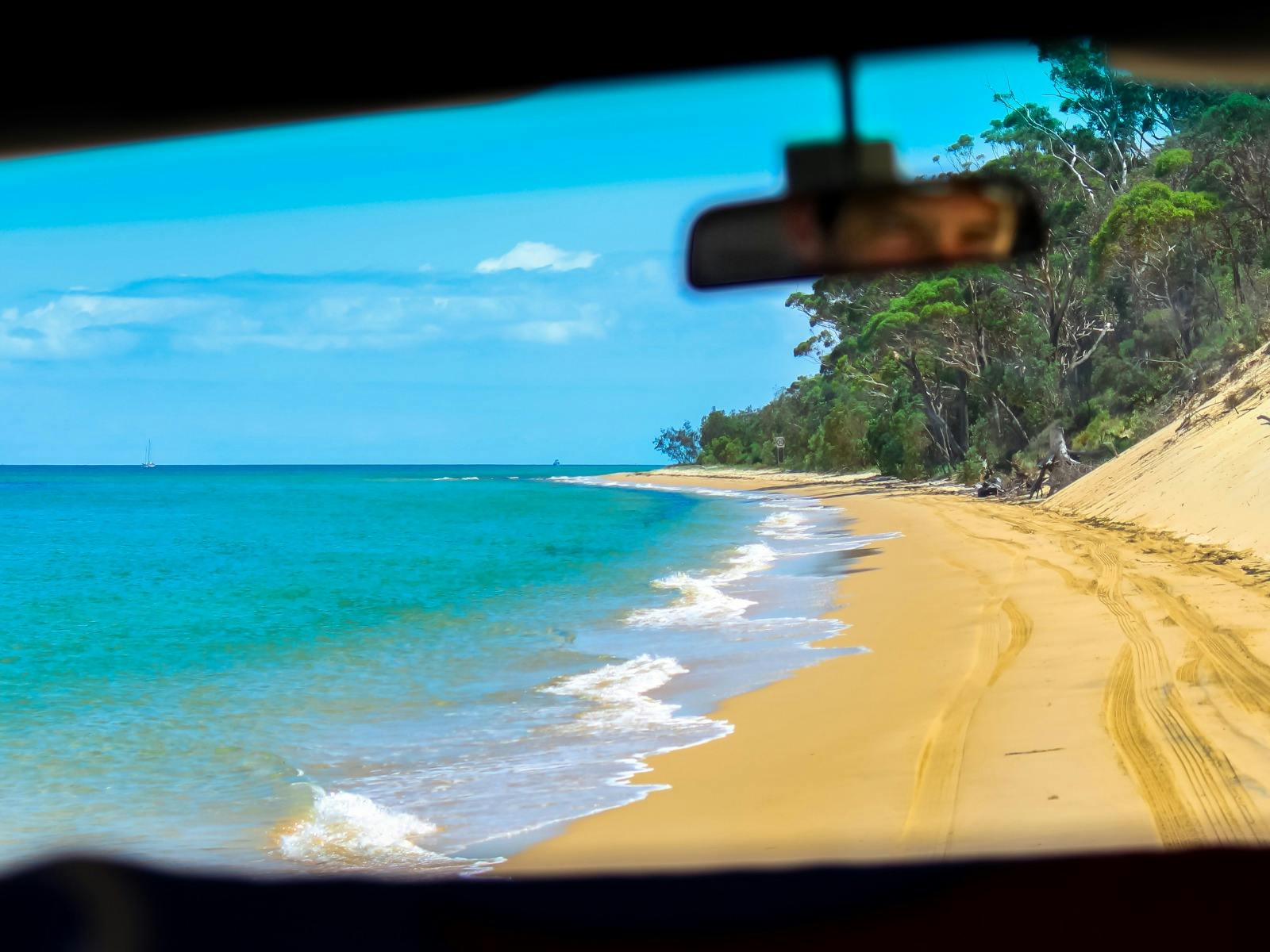 從車內看到的景色，沿著金色的沙灘和清澈的藍色海水行駛