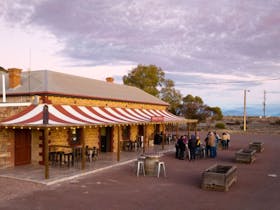people gather at dusk under the striped verandah of the Prairie Hotel