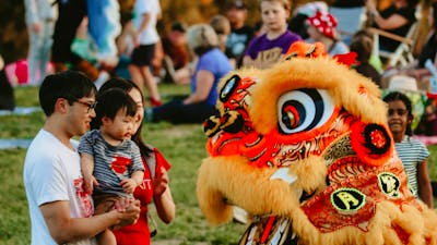 Image of a dragon dancer greeting a man and baby
