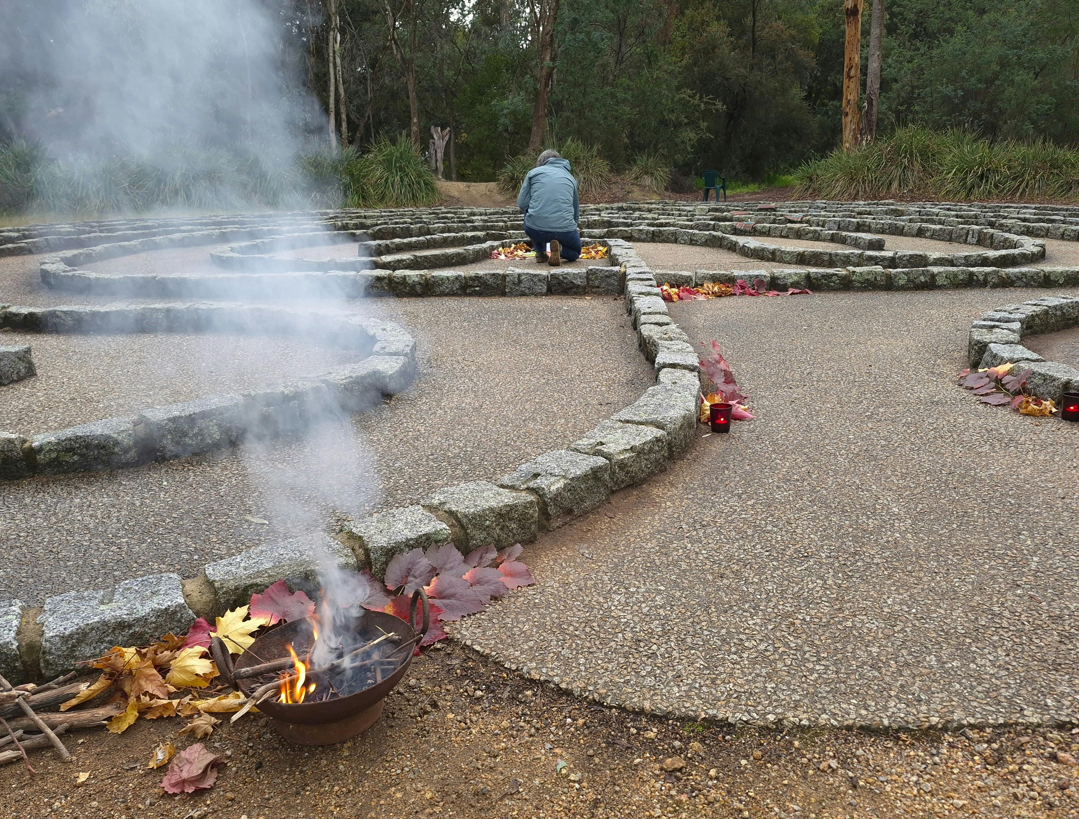Participant at the Beechworth labyrinth centre with ritual fire, smoke and autumn leaves.