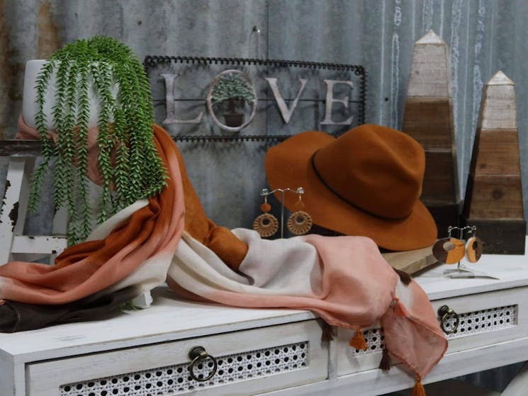 White cupboard with a brown hat, green plant, pink, white and brown scarves and various home décor.