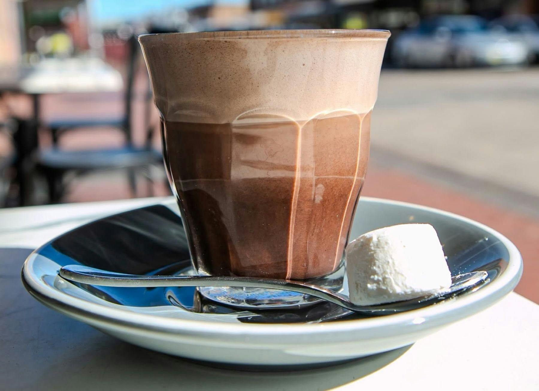 A coffee in a glass on a saucer with a marshmallow outside El Latte Lithgow.