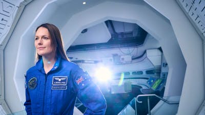 A woman at a space station wearing a blue astronaut uniform