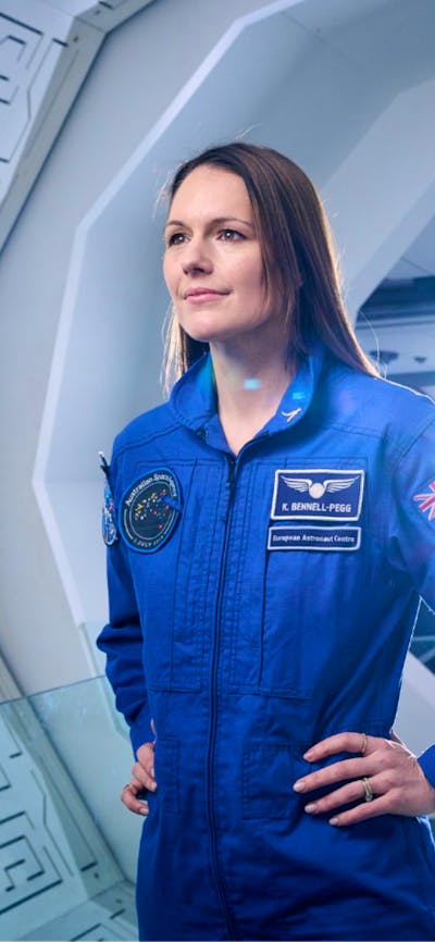 A woman at a space station wearing a blue astronaut uniform