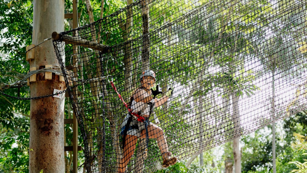 Woman climbing through a net obstacle on the high ropes park surrounded by lush rainforest