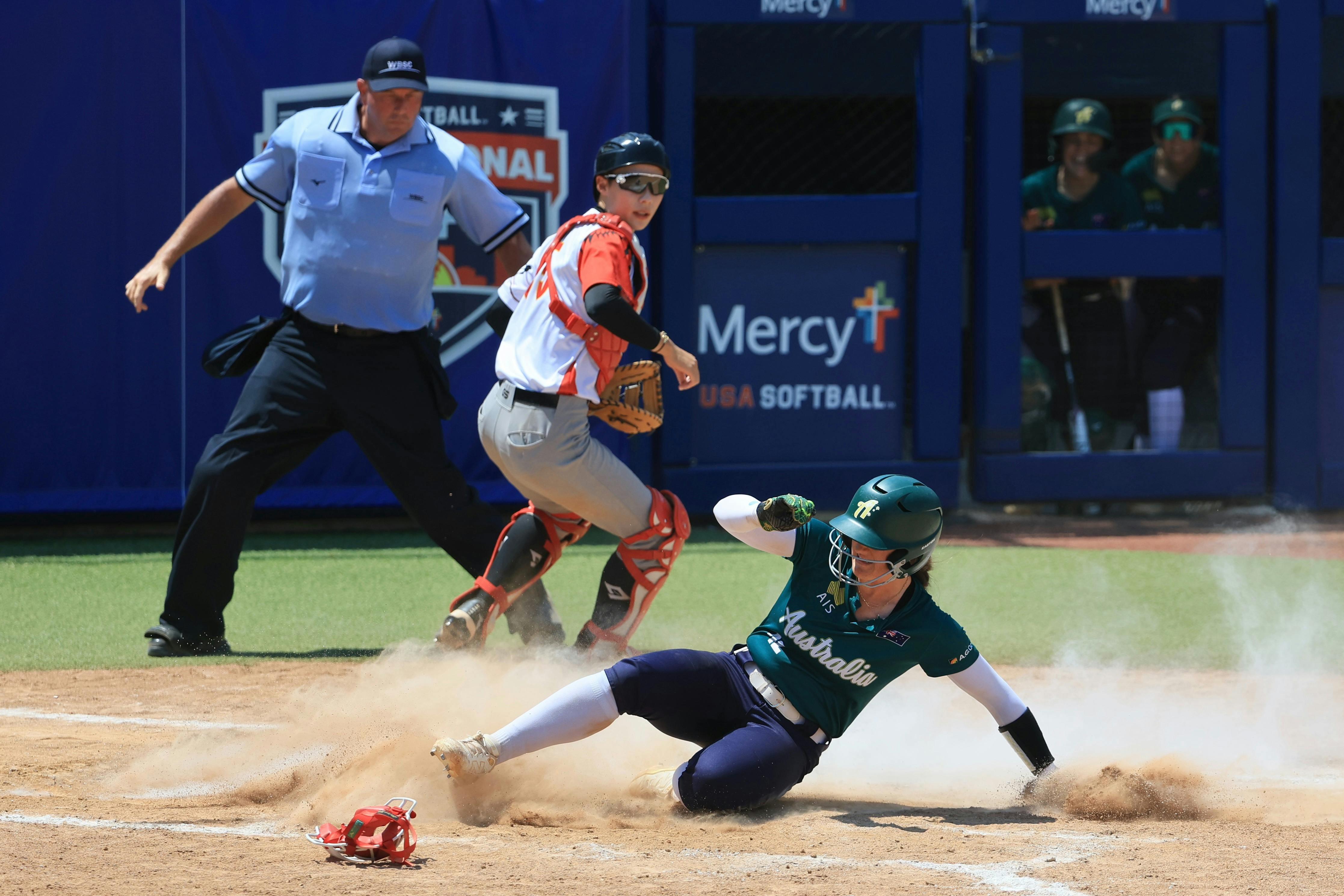 Australian runner slides home as catcher and umpire track the play at the plate.