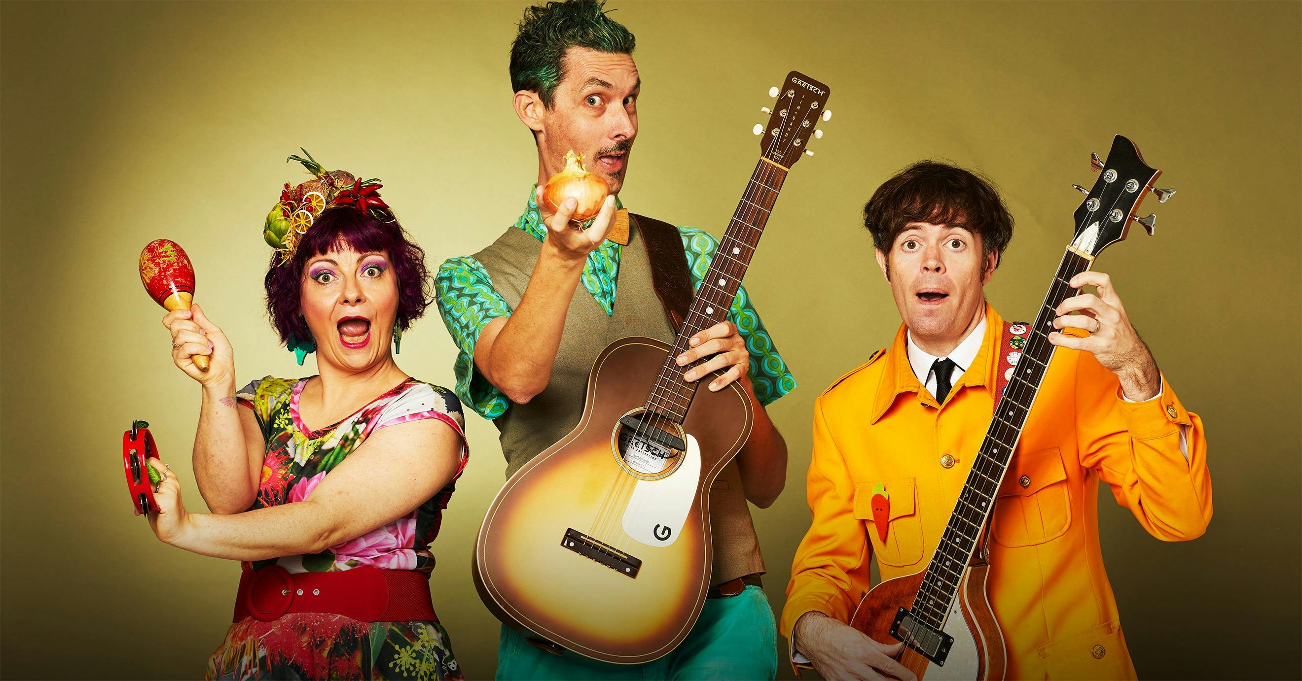 A kids band with 3 band members holding guitars and maracas, pulling silly faces