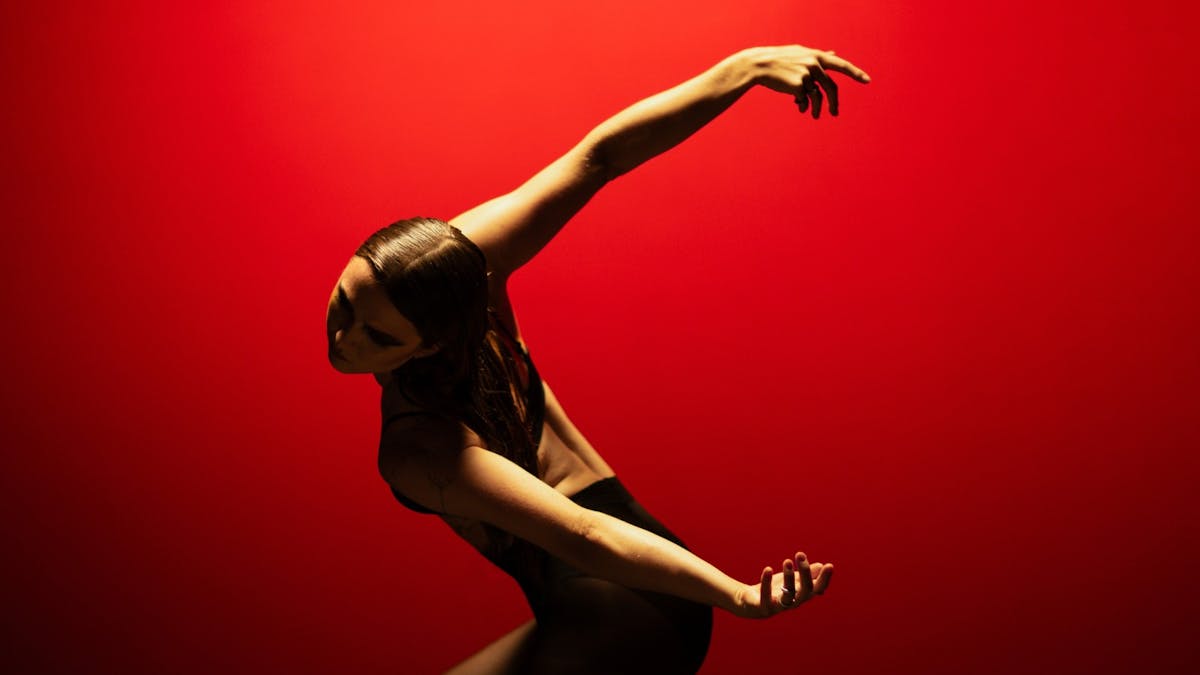 Dancer posed with arms outstretched behind them in front of a bright red backdrop.