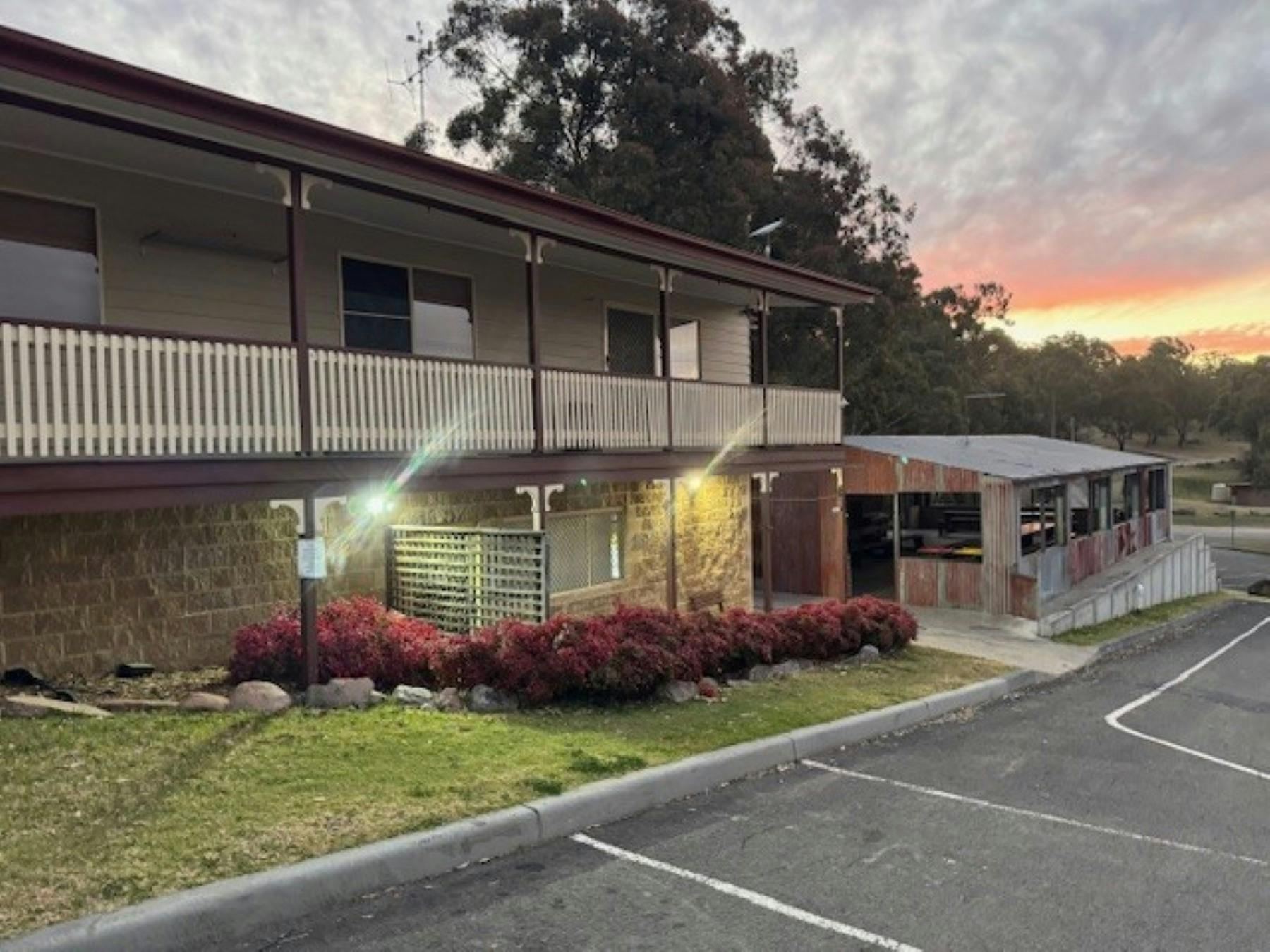 A two story building with red shrubbery at the front of the lower floor and a corrugated iron shed