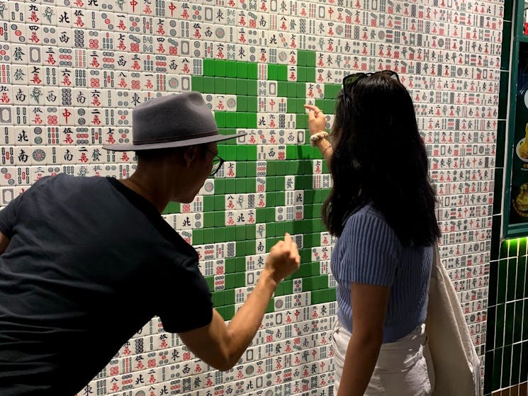 Two friends pointing at a mahjong wall