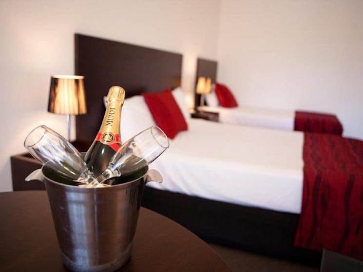 Champagne bottle and two glasses in ice bucket with two beds behind