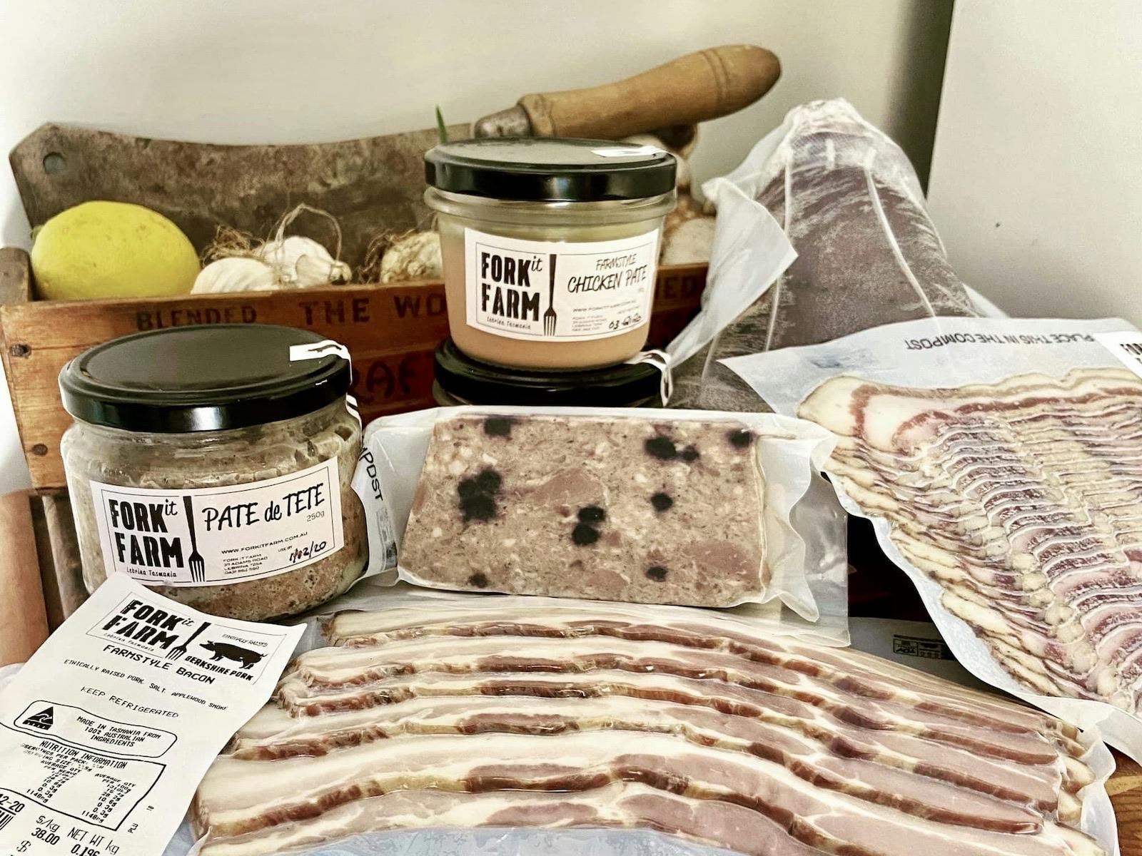 A variety of Fork it Farm artisanal meats, pâtés, and bacon arranged on a wooden crate for display.
