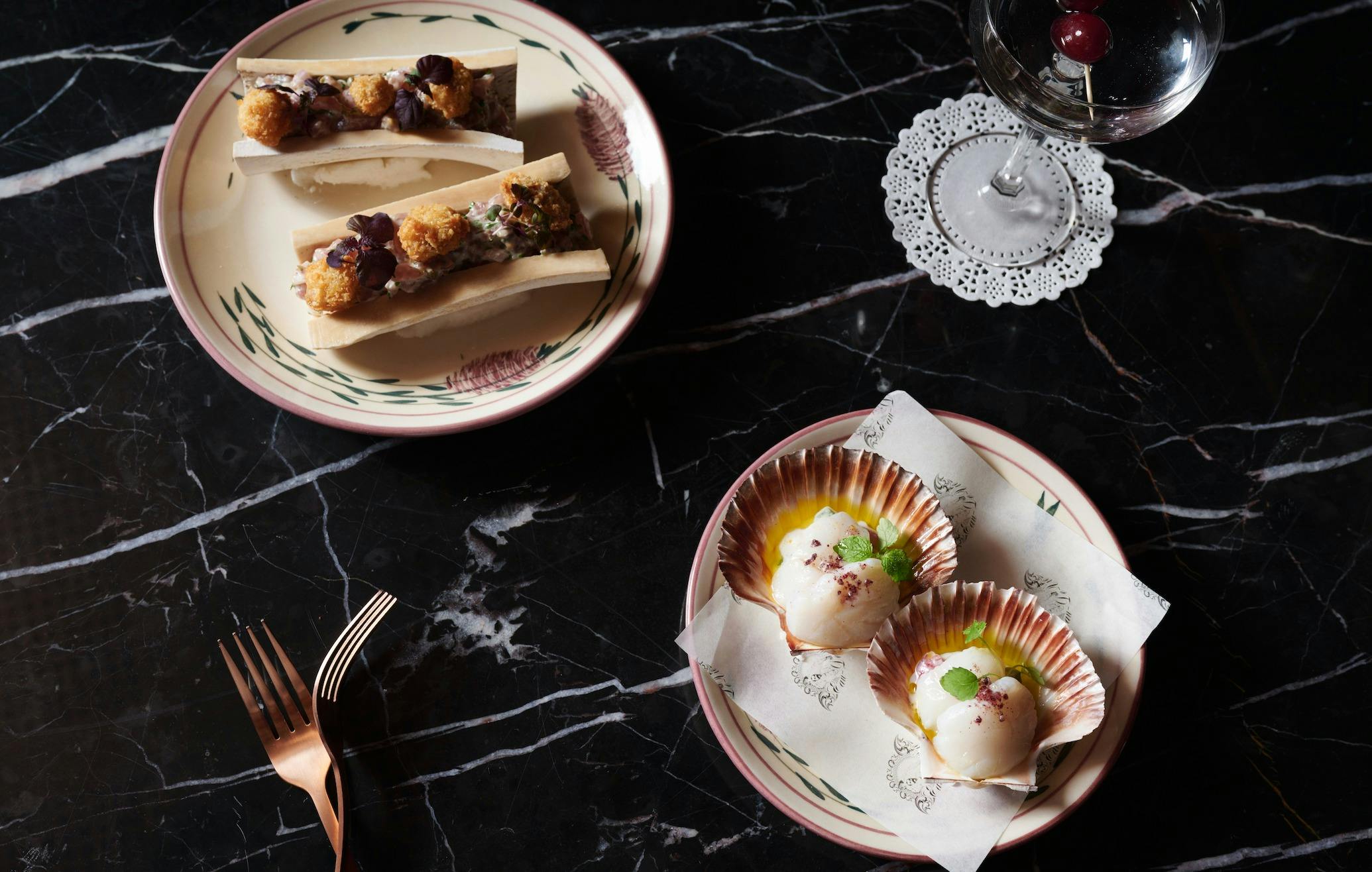 Two plates of food and a martini set on a marble table