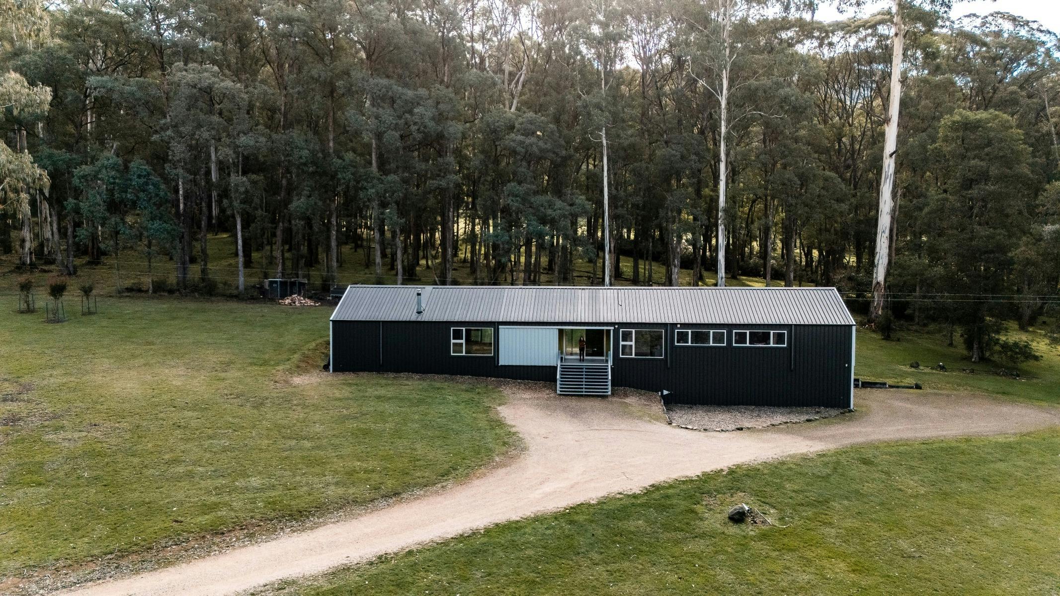Overhead drone image of long house clad in monument cladding,  surrounded by green bushland