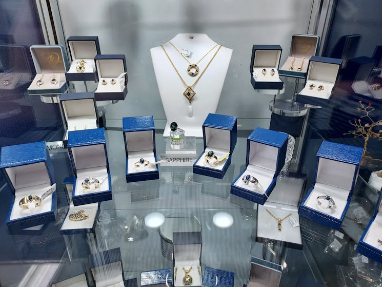 Sapphire Jewellery displayed on glass shelf in cabinet.