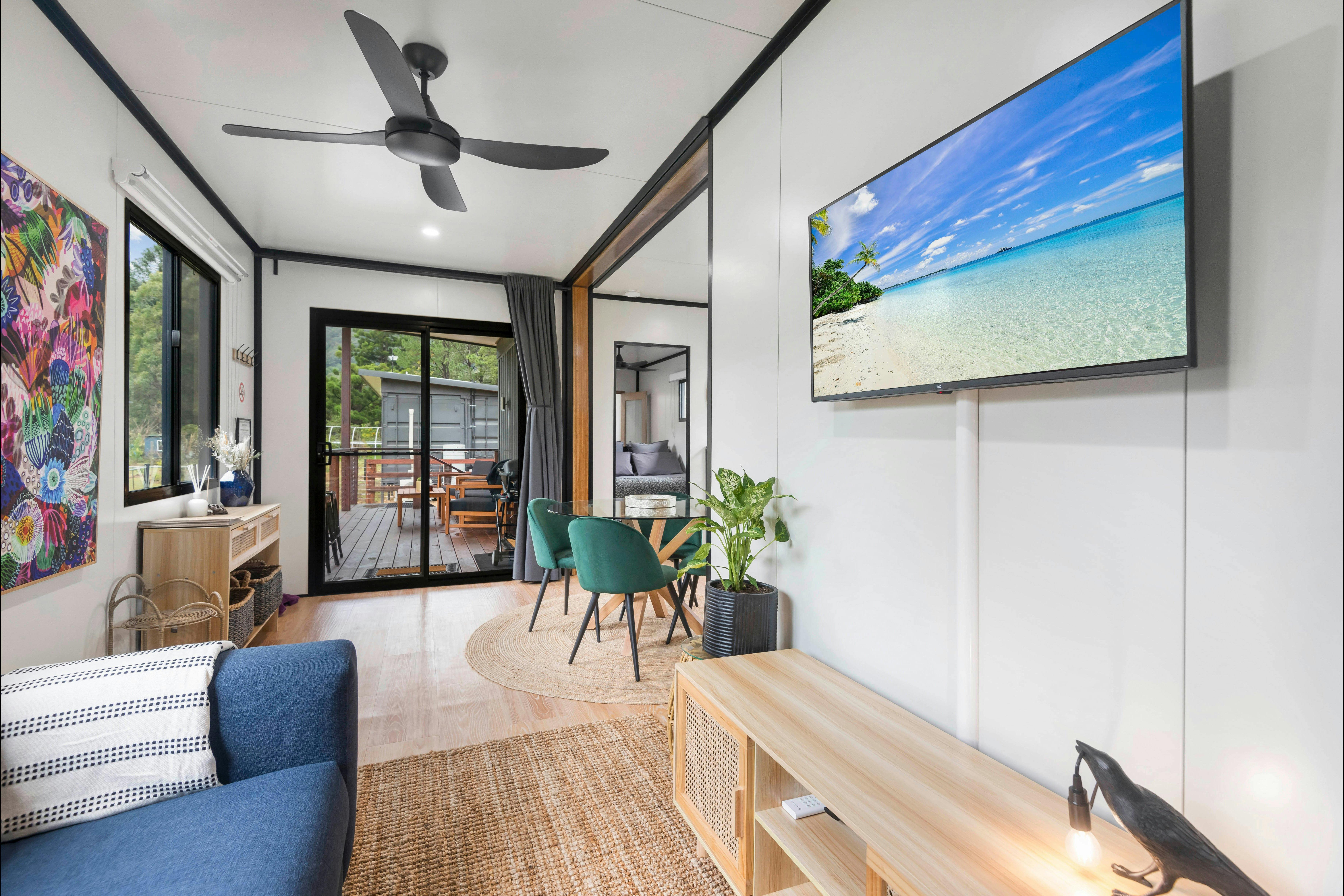 Lounge room with comfortable lounge and TV, looking towards the deck and dining area of the cottage