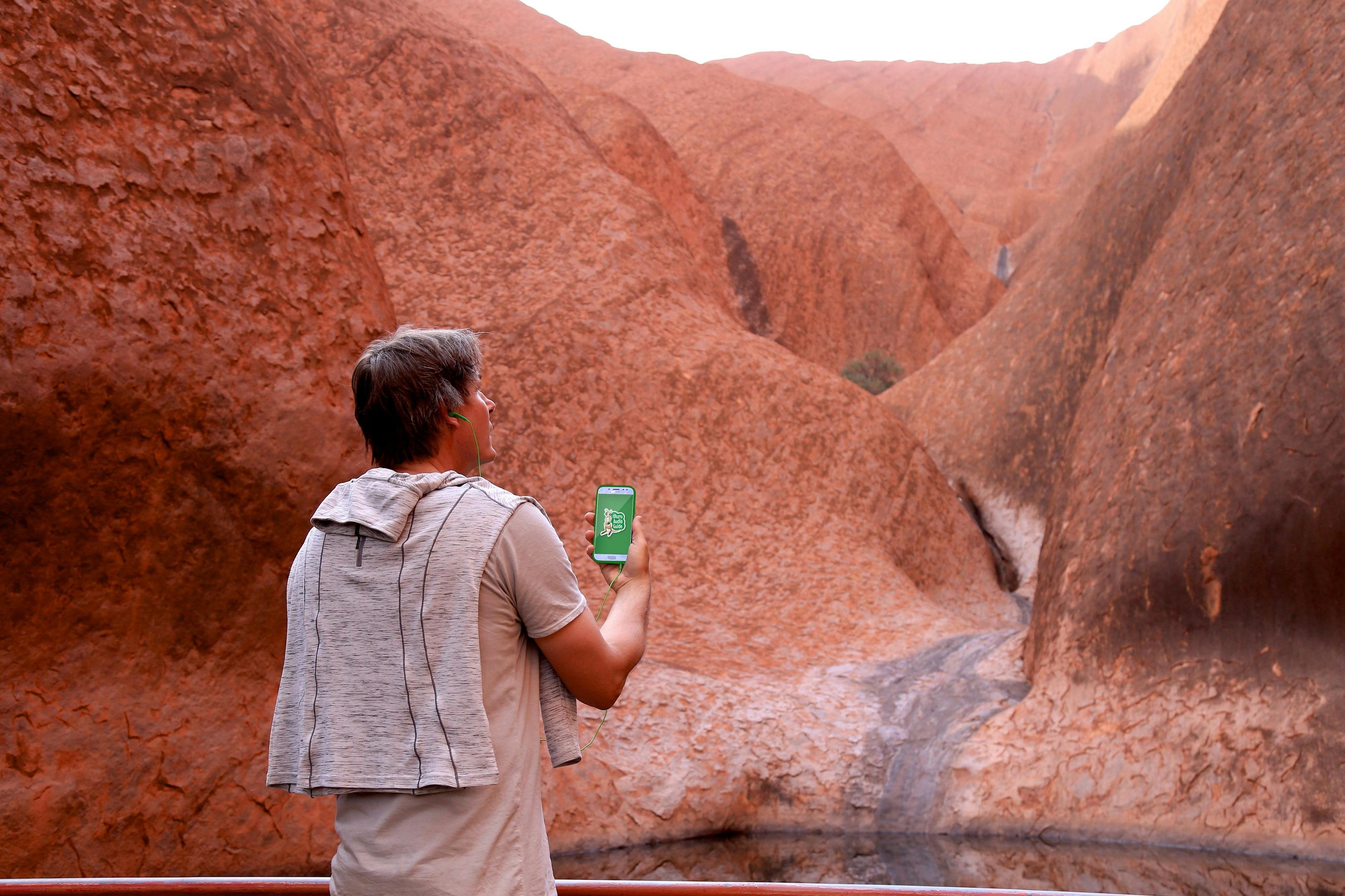 A man stands at Uluru and is  mesmerised by the audio guide he is listening to.