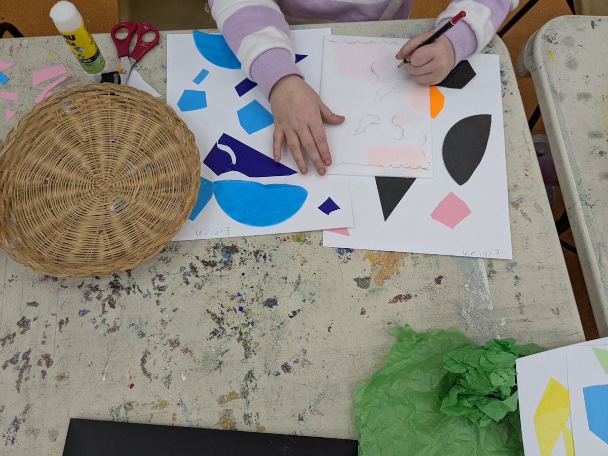 A young child creates a collage with coloured paper shapes and pencils