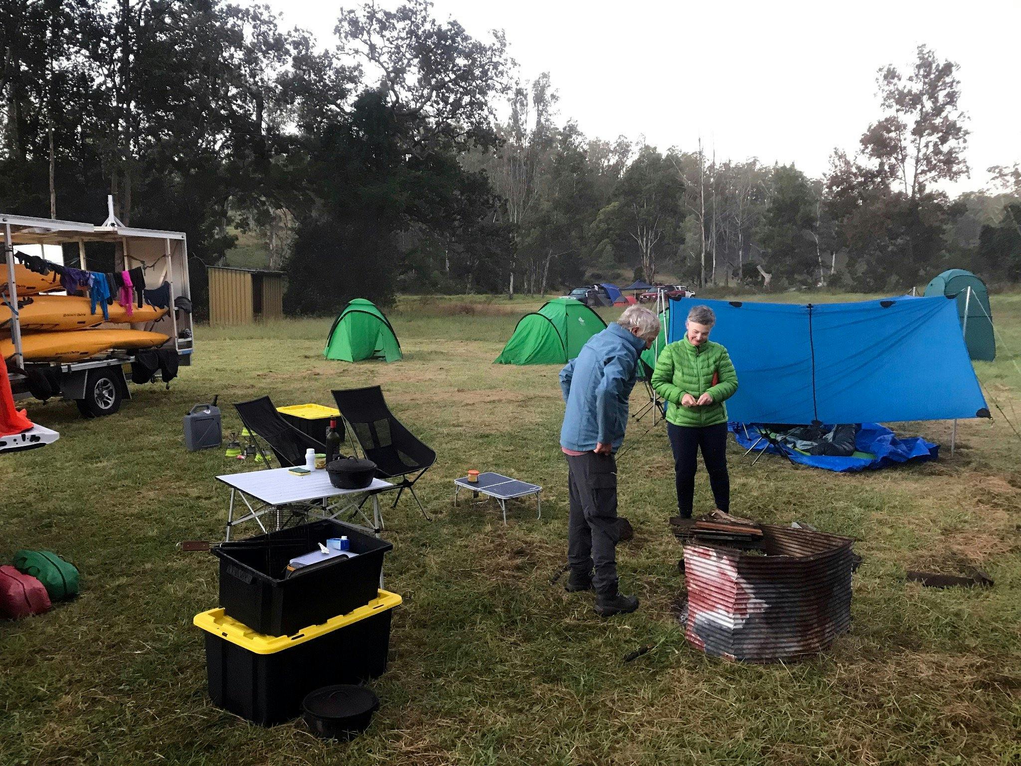 Two people are standing next to a campfire with tents in the background on a Kayak tour.