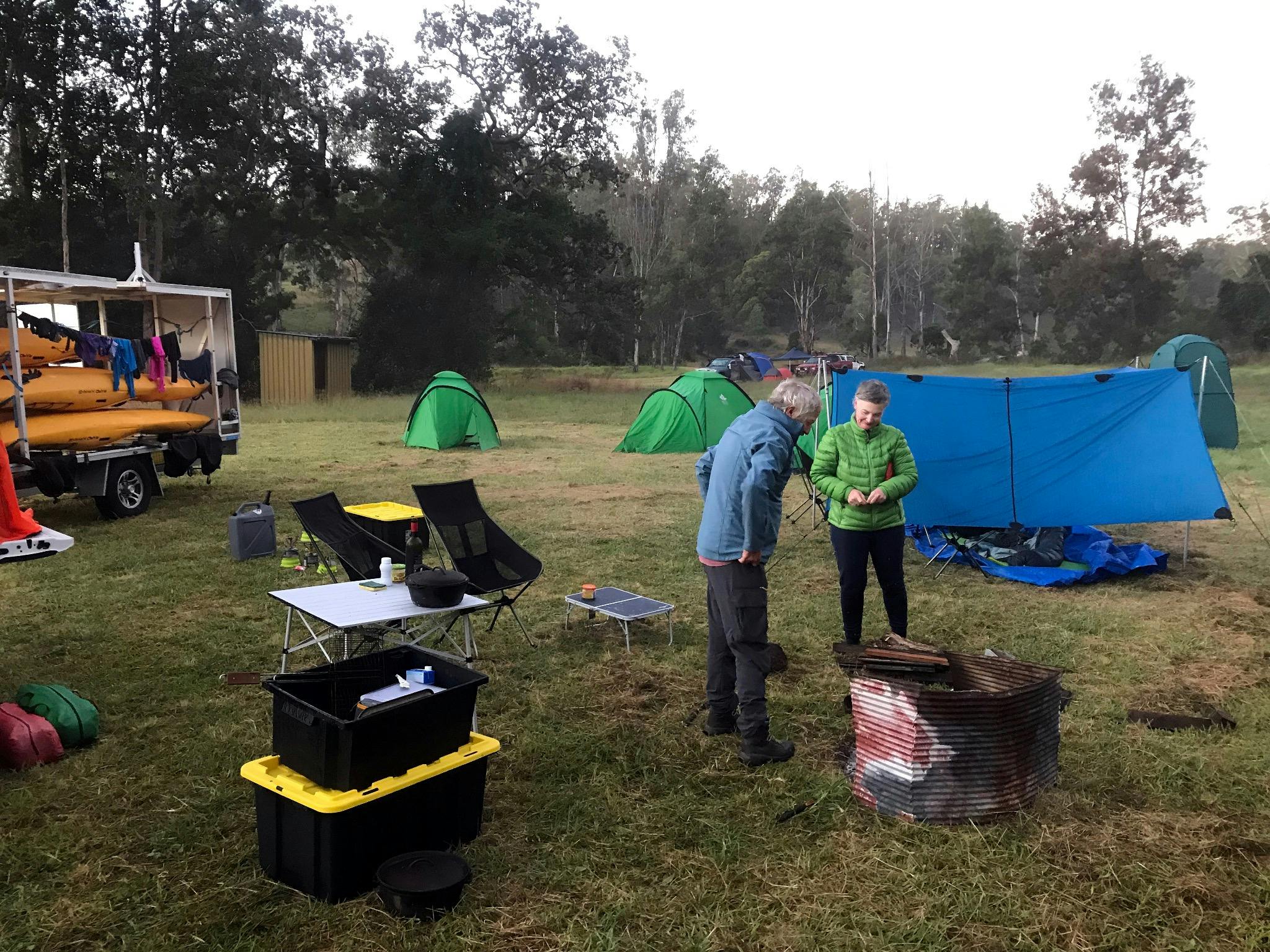 Two people are standing next to a campfire with tents in the background on a Kayak tour.