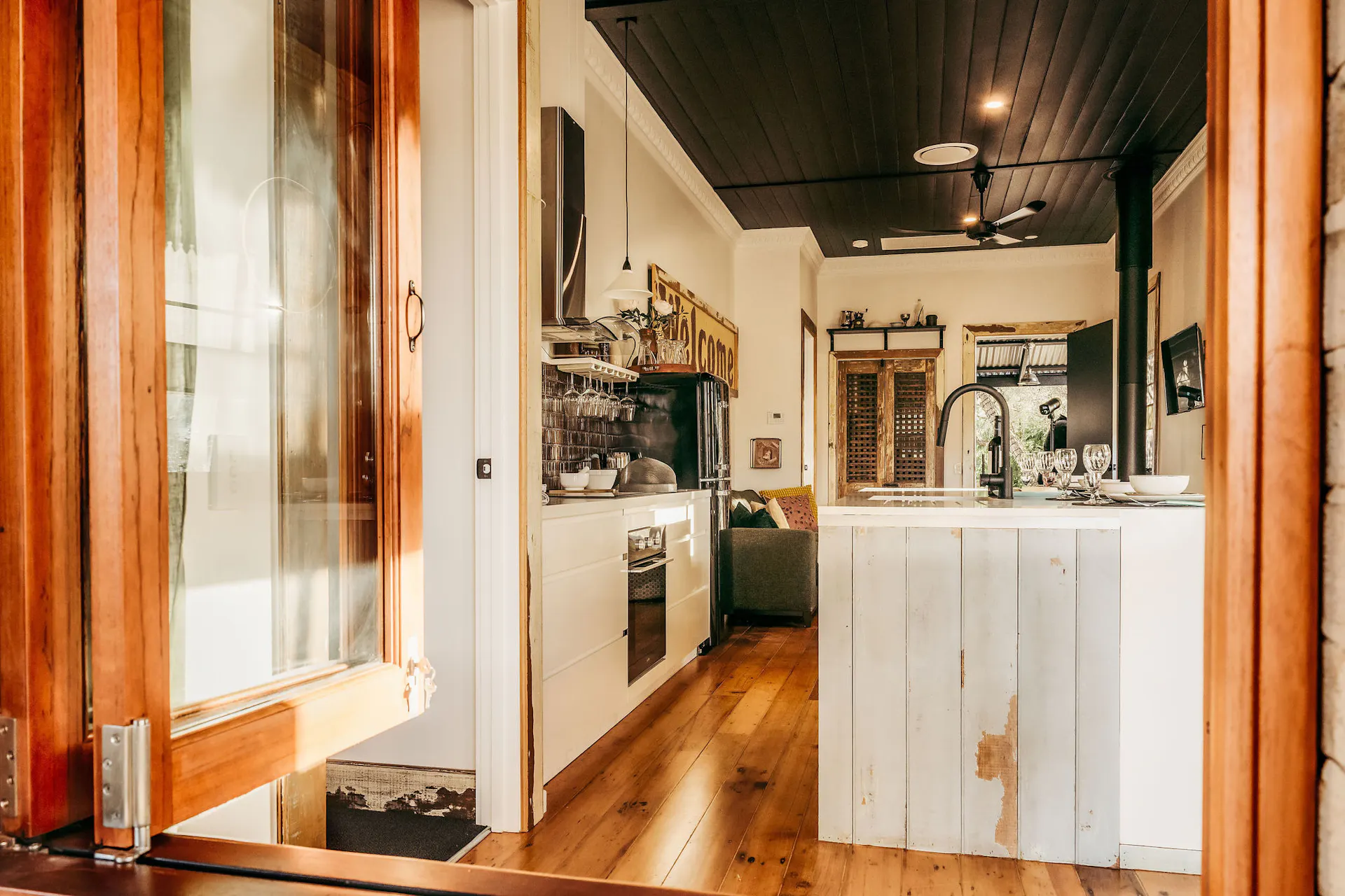 Kitchen and Living Area viewed through an opend timber bi-fold window. Black ceiling featured.