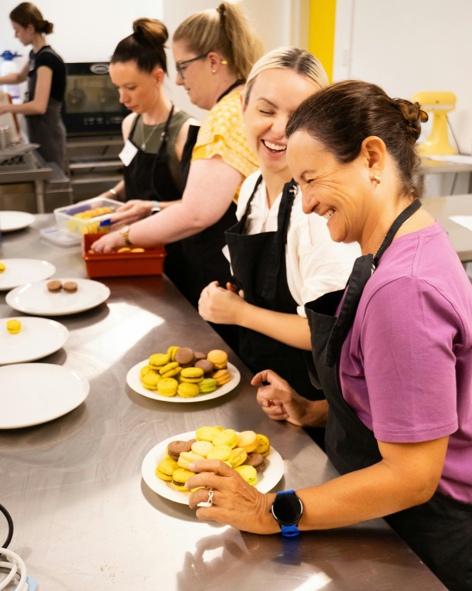 2 people in a kitchen laughing and enjoying the a French Macarons they made