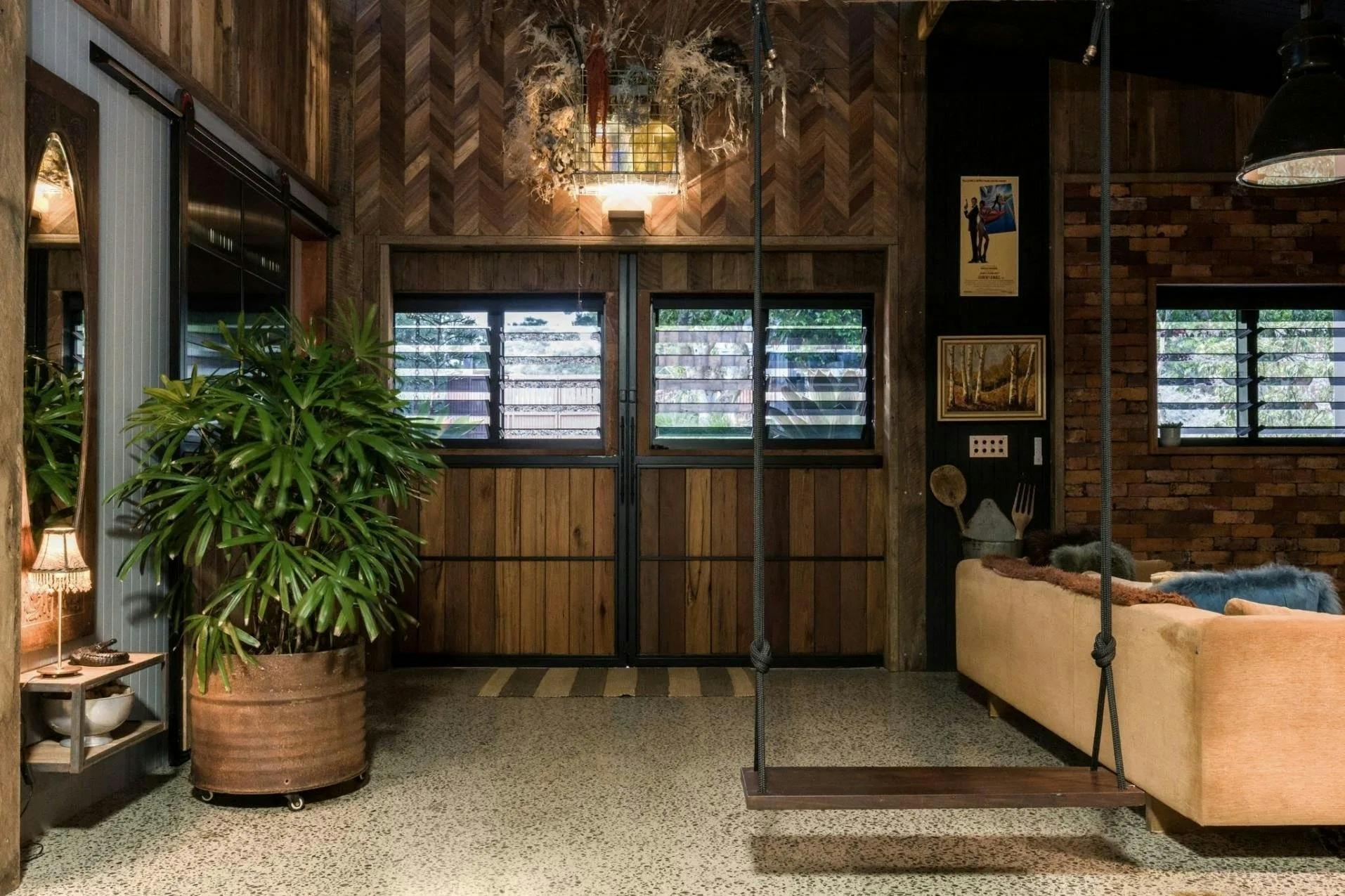 Open-plan barn interior with timber walls, a hanging swing seat and large indoor plants