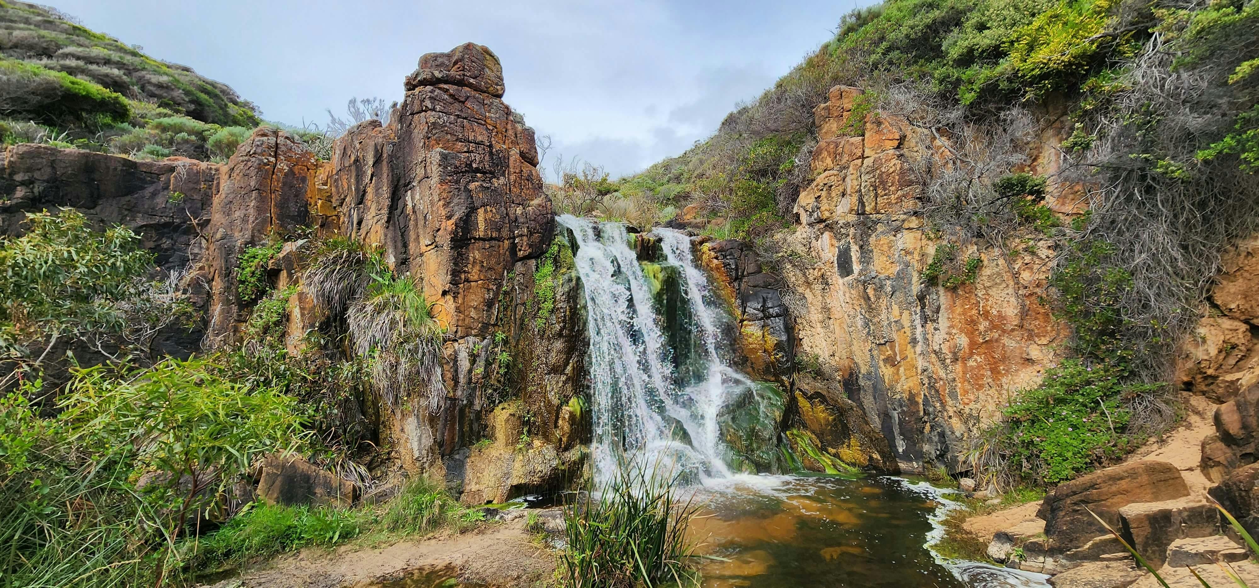 Australian landscape of flowing waterfall surrounded by red rocks and hills